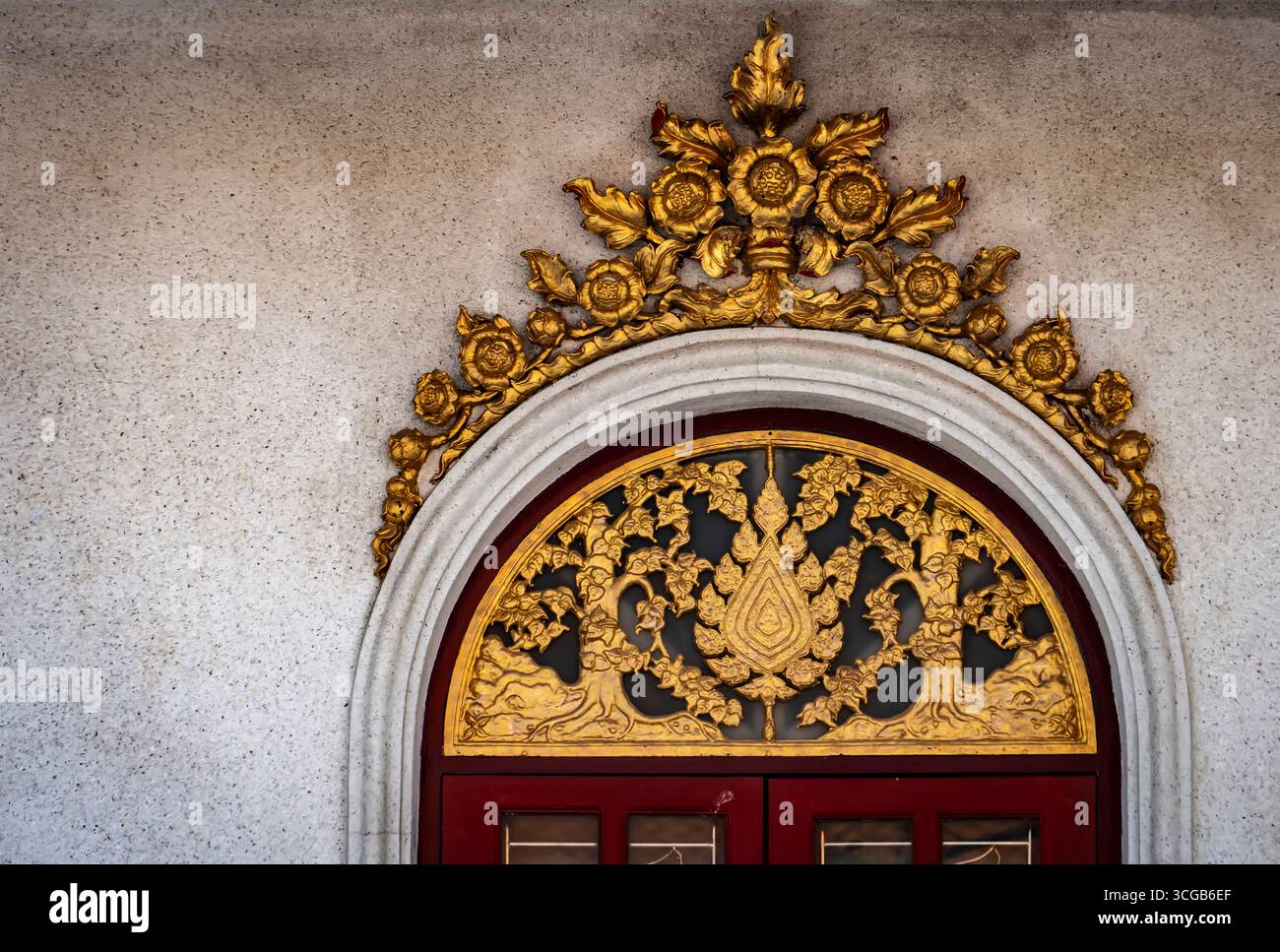 Arco dorato ornato sopra una porta rossa, intricati motivi floreali e a foglia, sfondo grigio testurizzato della parete Foto Stock