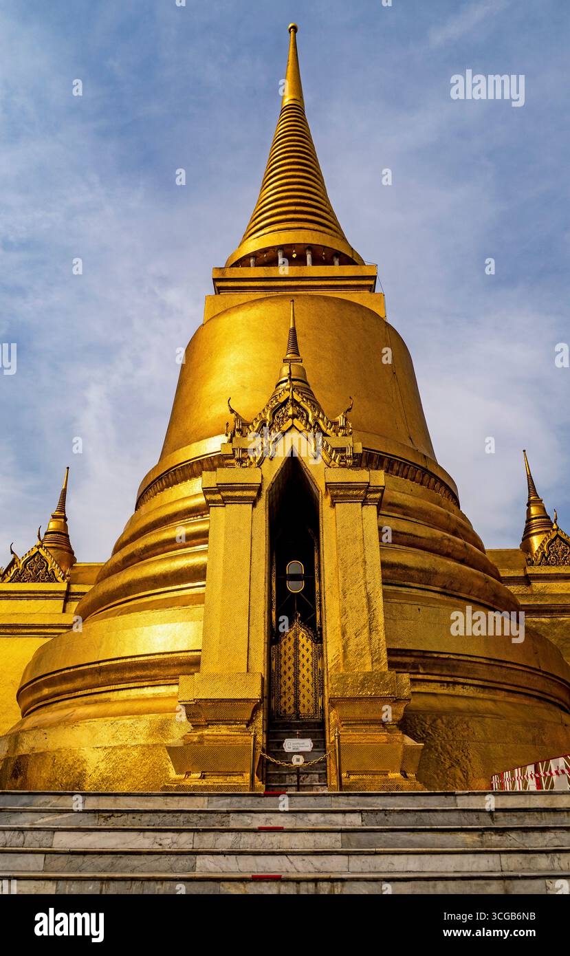 Un maestoso stupa dorato con una guglia appuntita, adagiato su un cielo nuvoloso, che mette in mostra dettagli architettonici complessi Foto Stock