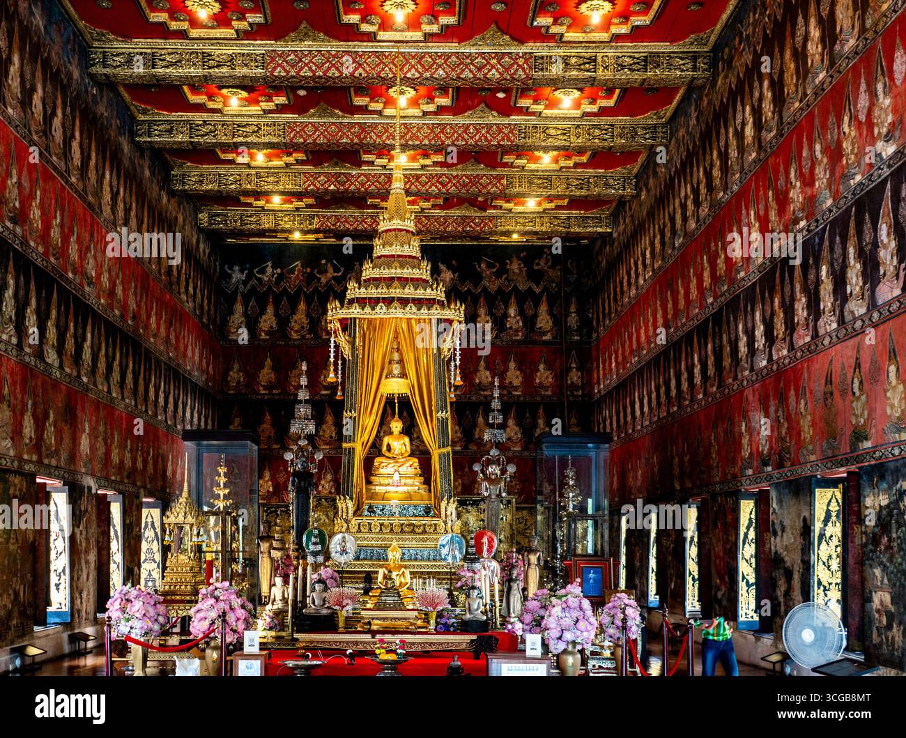 Un tempio interno splendidamente decorato caratterizzato da una statua dorata di Buddha circondata da architetture ornate e composizioni floreali Foto Stock