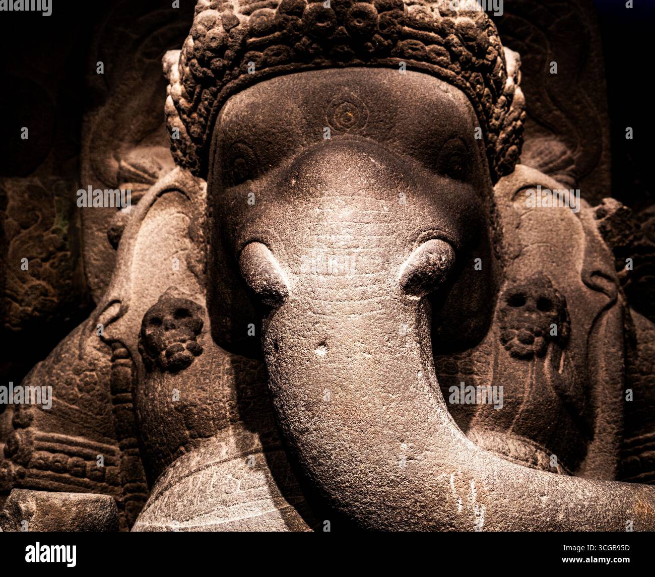 Una vista ravvicinata di una scultura in pietra di una divinità dalla testa di elefante, che mostra intricate incisioni e texture, con un'illuminazione spettacolare Foto Stock