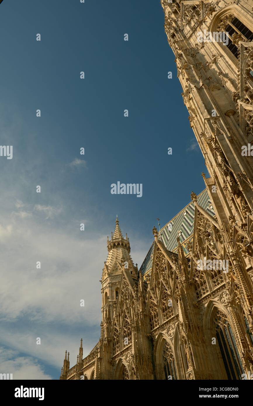 Vista dal basso della cattedrale di Santo Stefano a Vienna con la sua facciata gialla illuminata dal sole sulla destra e il cielo azzurro con nuvole sulla sinistra. Foto Stock