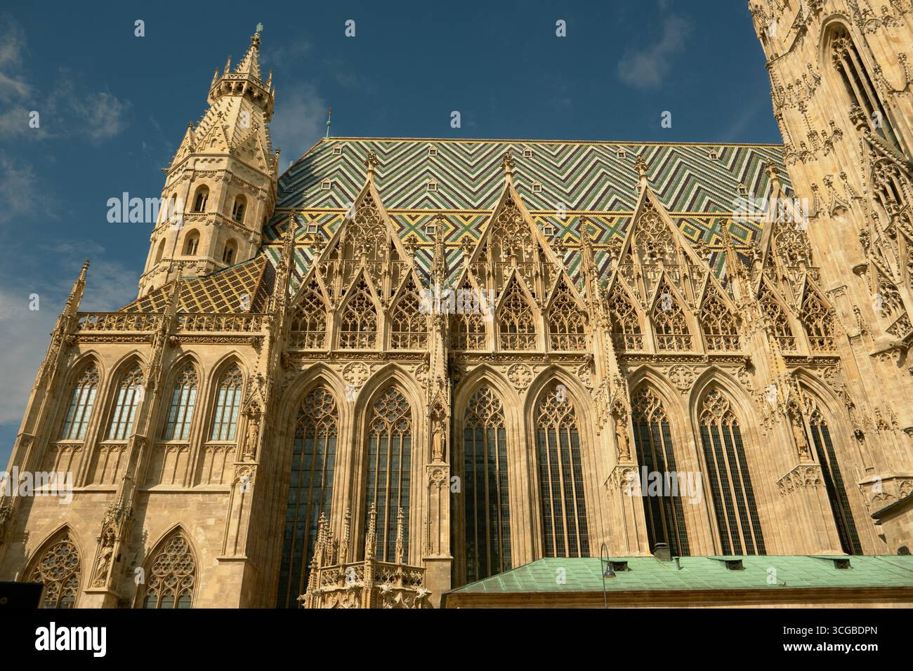 Vista laterale della Cattedrale di Santo Stefano di Vienna, con grandi vetrate colorate, guglie torreggianti e il colorato tetto a mosaico su un luminoso edificio Foto Stock