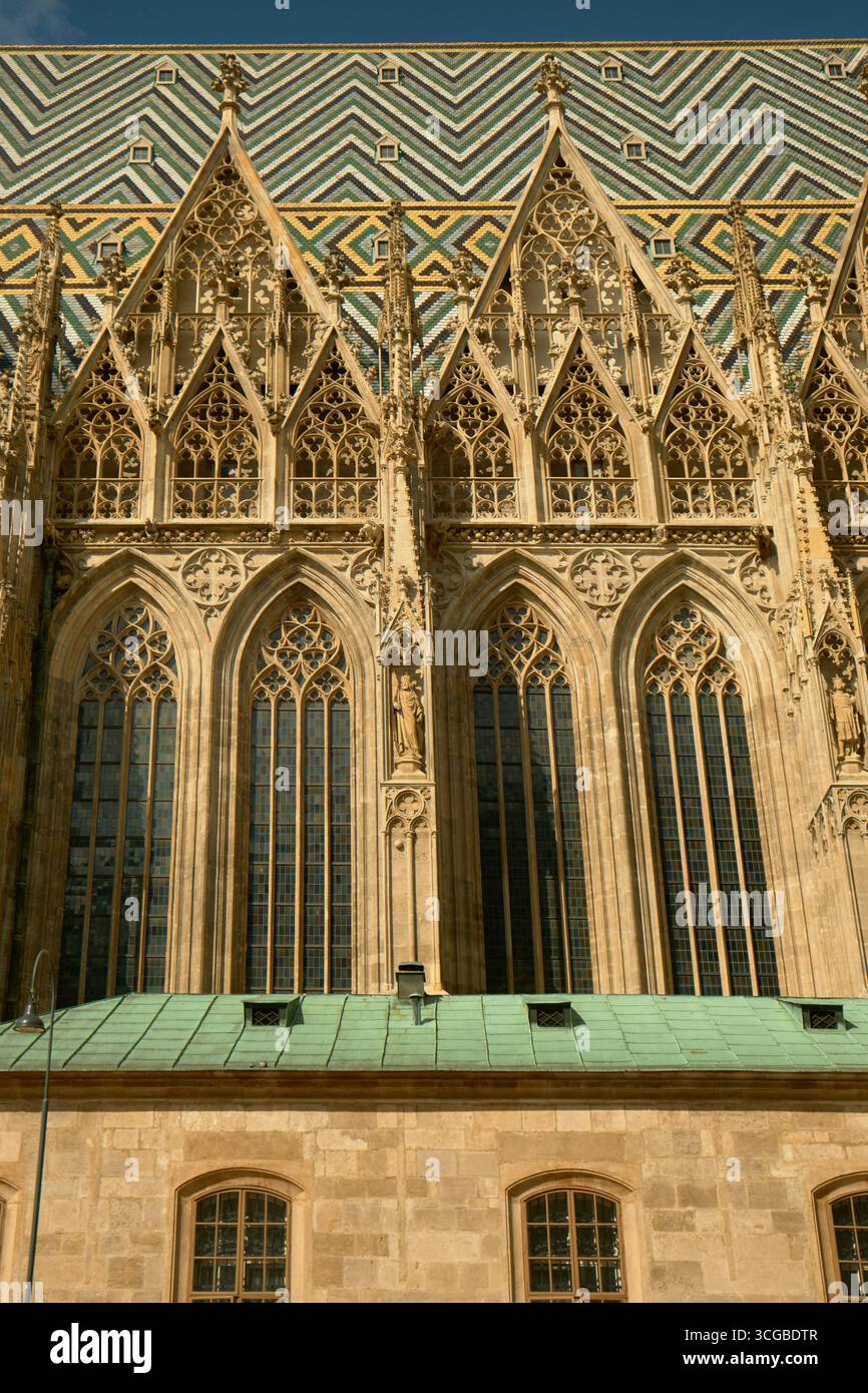 Vista laterale della cattedrale di Santo Stefano di Vienna con tetto piastrellato colorato, finestre gotiche a punta con riquadri in pietra e contrafforti di sostegno e Foto Stock