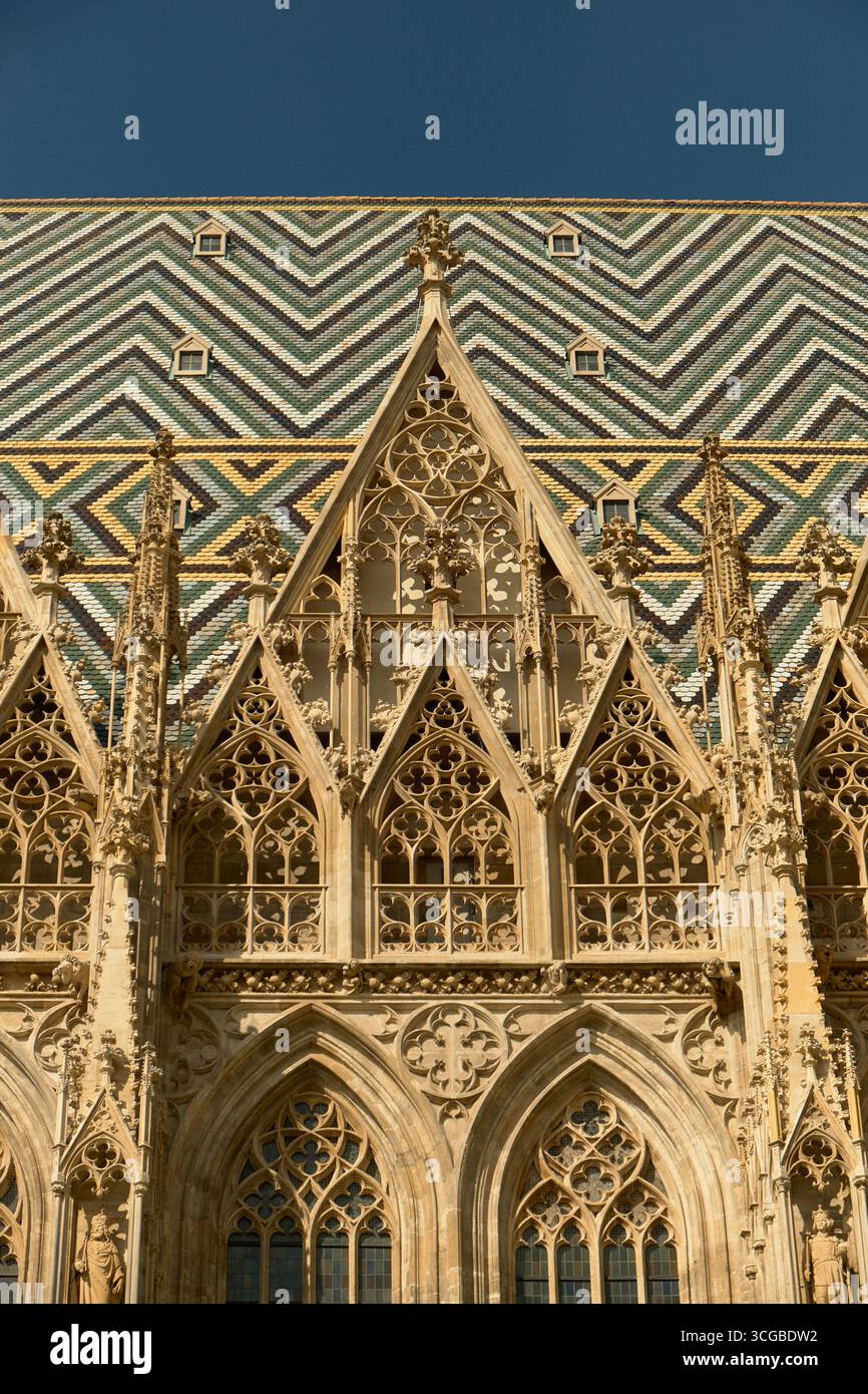 Facciata superiore della cattedrale di Santo Stefano di Vienna con intricate finestre gotiche a punta con trafori in pietra e un vivace tetto piastrellato geometrico a yel Foto Stock