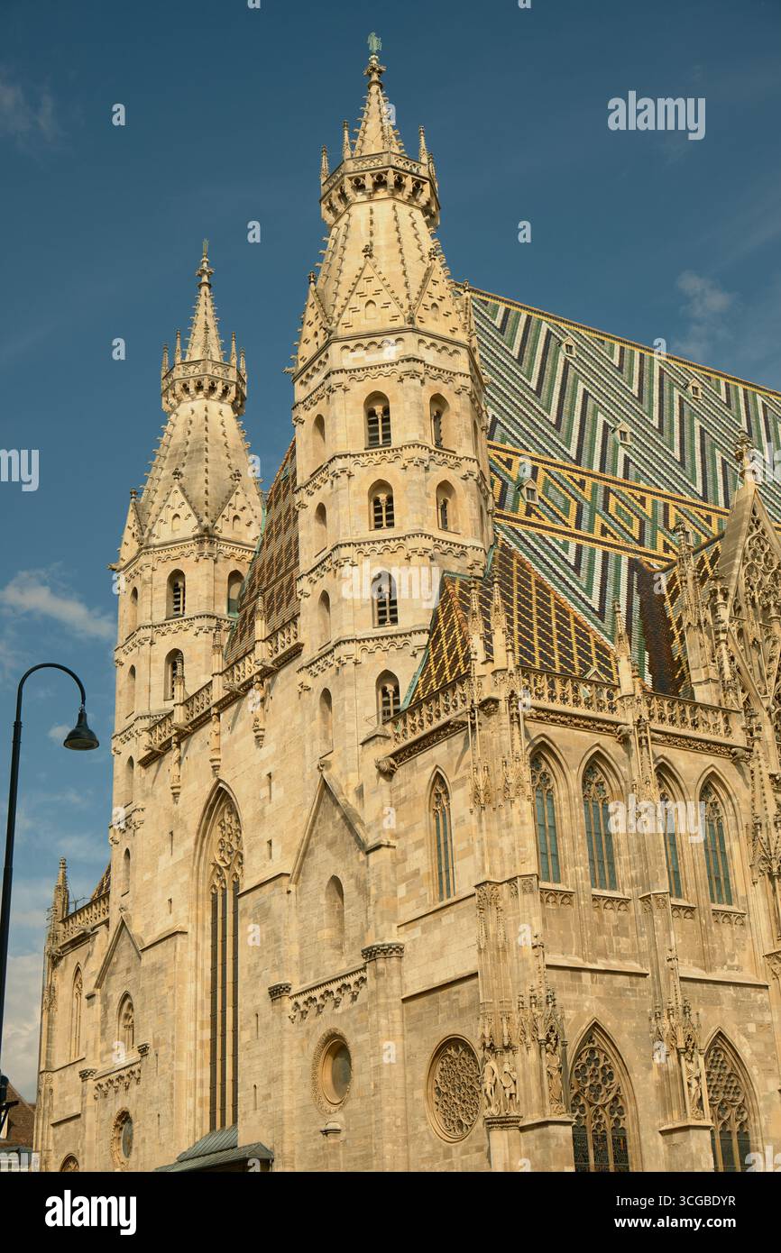 Vista frontale e laterale della cattedrale di Santo Stefano a Vienna, con dettagli gotici e tetto a mosaico, con un'unica lampada nera sul lato sotto una Foto Stock