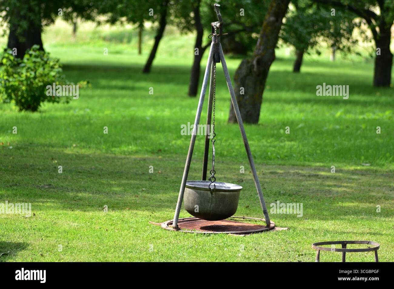 Cavalletto in metallo con telo appeso in un giardino erboso. Tradizionale attrezzatura da cucina all'aperto utilizzata per caminetti, picnic e vita rustica in campagna Foto Stock