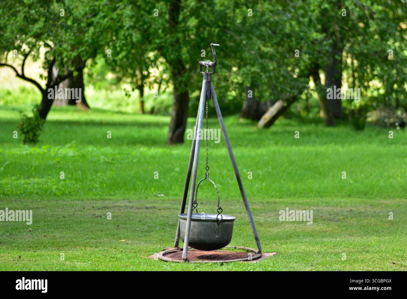 Cavalletto in metallo con telo appeso in un giardino erboso. Tradizionale attrezzatura da cucina all'aperto utilizzata per caminetti, picnic e vita rustica in campagna Foto Stock