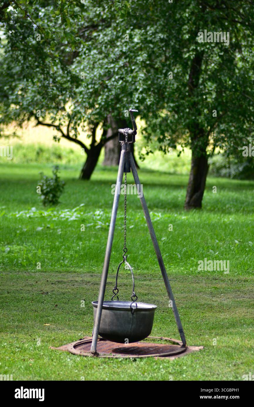 Cavalletto in metallo con telo appeso in un giardino erboso. Tradizionale attrezzatura da cucina all'aperto utilizzata per caminetti, picnic e vita rustica in campagna Foto Stock