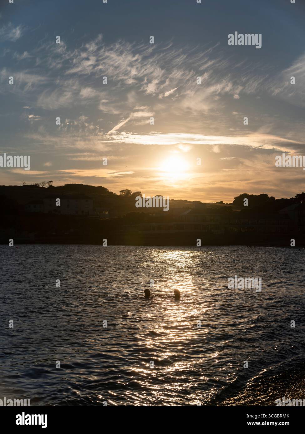 Due persone nuotano in mare durante un tramonto estivo a Freshwater Bay sull'isola di Wight. Foto Stock