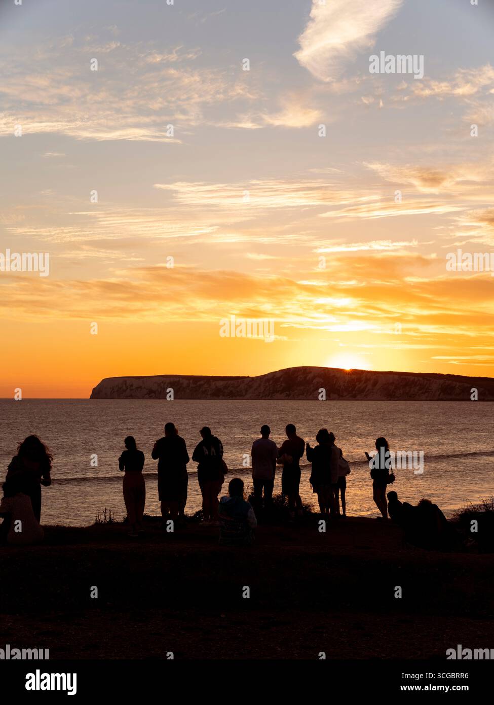Silhouette di persone che guardano il tramonto sulla baia di Compton sull'isola di Wight in una serata estiva. Foto Stock