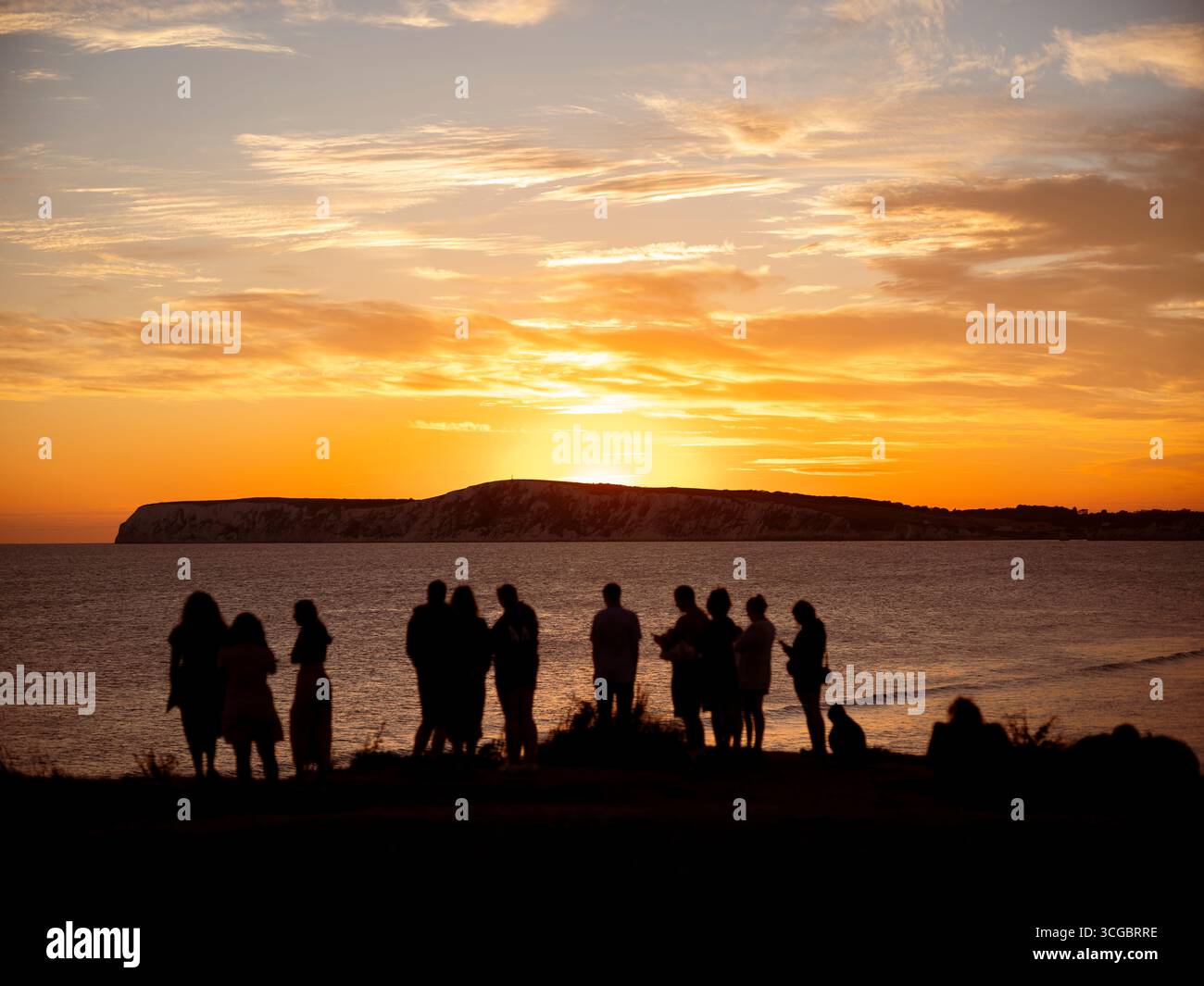 Silhouette di persone che guardano il tramonto sulla baia di Compton sull'isola di Wight in una serata estiva. Foto Stock