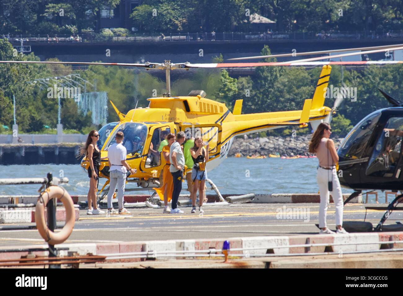 Un elicottero giallo su un eliporto con persone che si imbarcano al Downtown Skyport nel porto di New York in una giornata estiva di sole Foto Stock