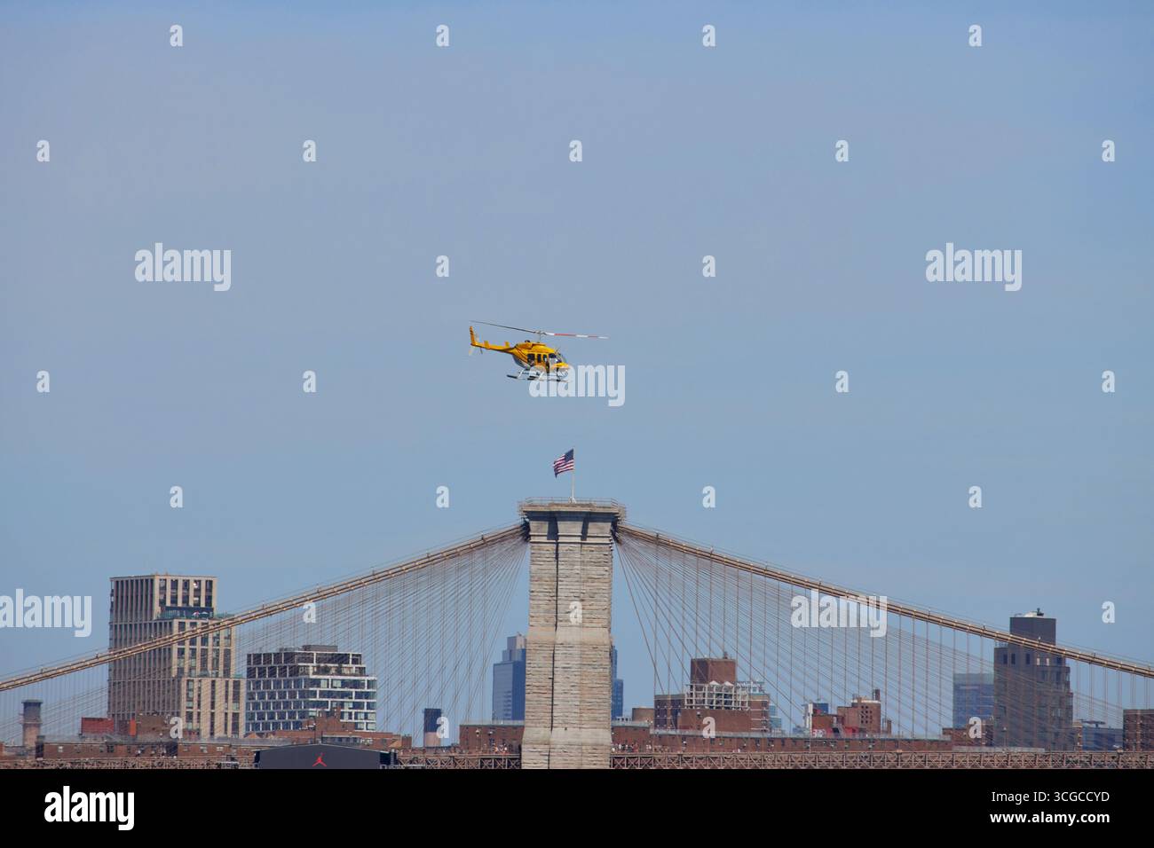 Un elicottero giallo sorvola il ponte di Brooklyn con una bandiera americana in cima in una giornata di sole con un cielo azzurro cristallino, copia spazio Foto Stock Un elicottero giallo sorvola il ponte di Brooklyn con una bandiera americana in cima in una giornata di sole con un cielo azzurro cristallino, copia spazio Foto Stock