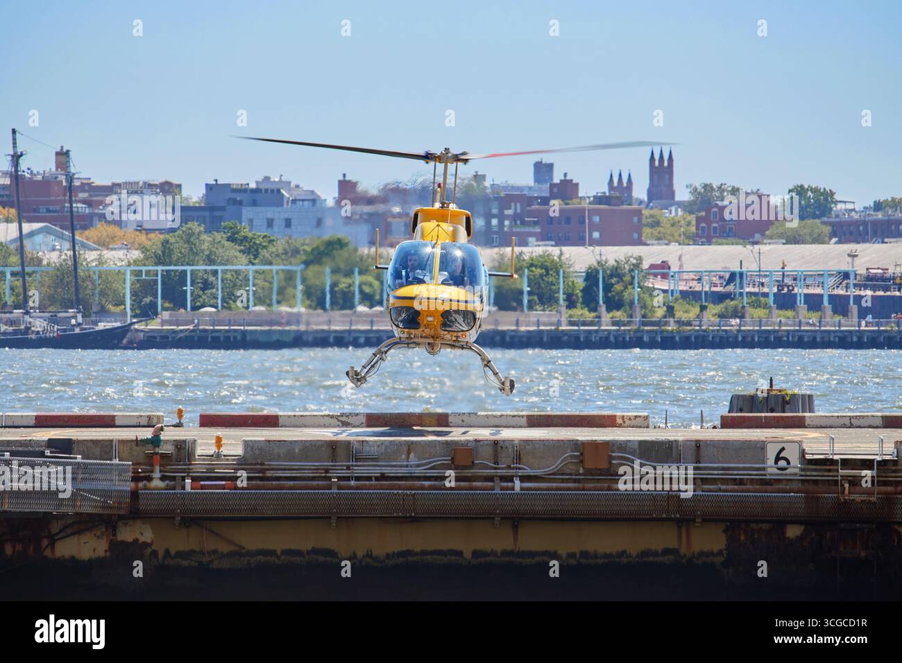 Un elicottero giallo di fronte che si libra appena sopra un eliporto durante l'atterraggio sul porto di New York in una soleggiata giornata estiva Foto Stock