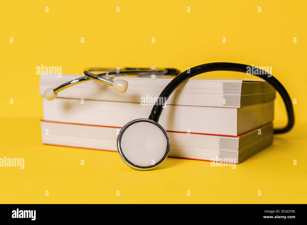 Stetoscopio appoggiato su libri di testo impilati su sfondo giallo brillante. Educazione medica. Foto Stock