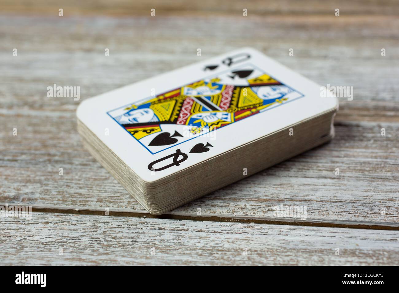 Vista ravvicinata di un mazzo di carte da gioco, con la carta della regina delle picche in cima, su un legno Foto Stock