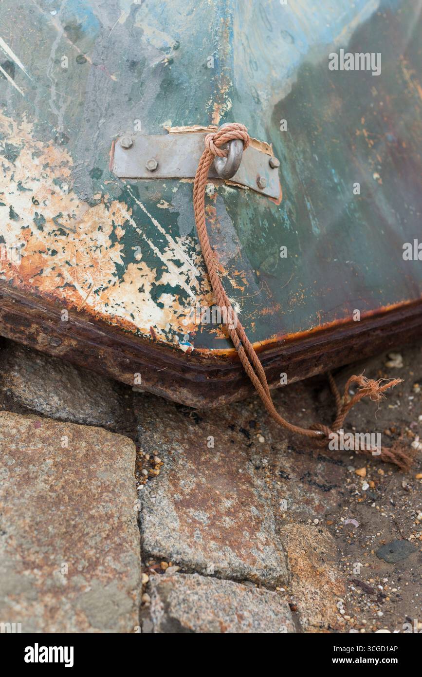 Prua usurata di una nave con vernice staccabile, ruggine visibile e vecchia fune legata a un gancio d'acciaio, evocando abbandono marittimo e ruvidità. Foto Stock