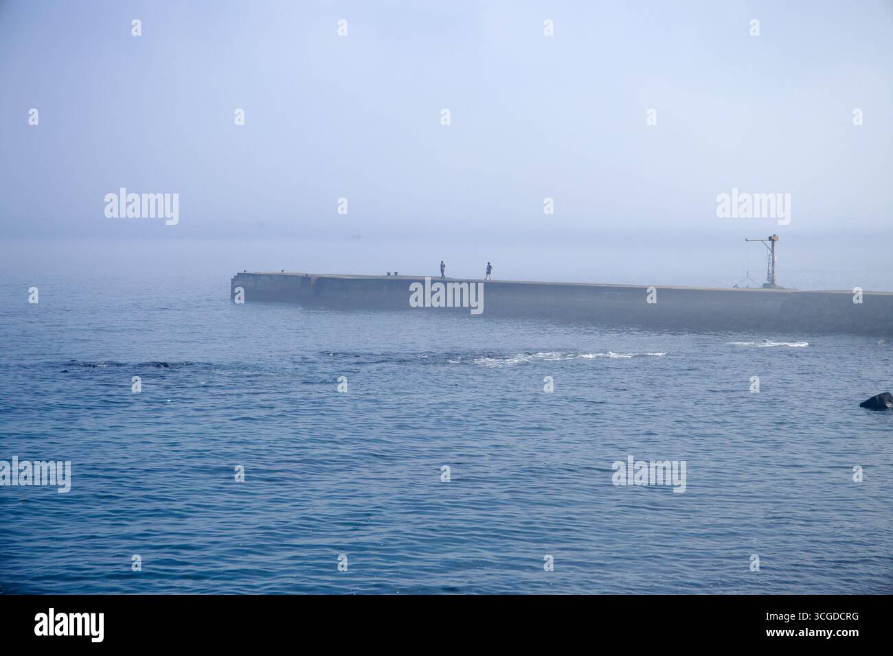 Un frangiflutti nebbioso si estende dalla costa vicino al Pan-Pacific Peace Park di Songaksan, con alcuni visitatori che camminano lungo il molo sopra le calme acque blu. Foto Stock