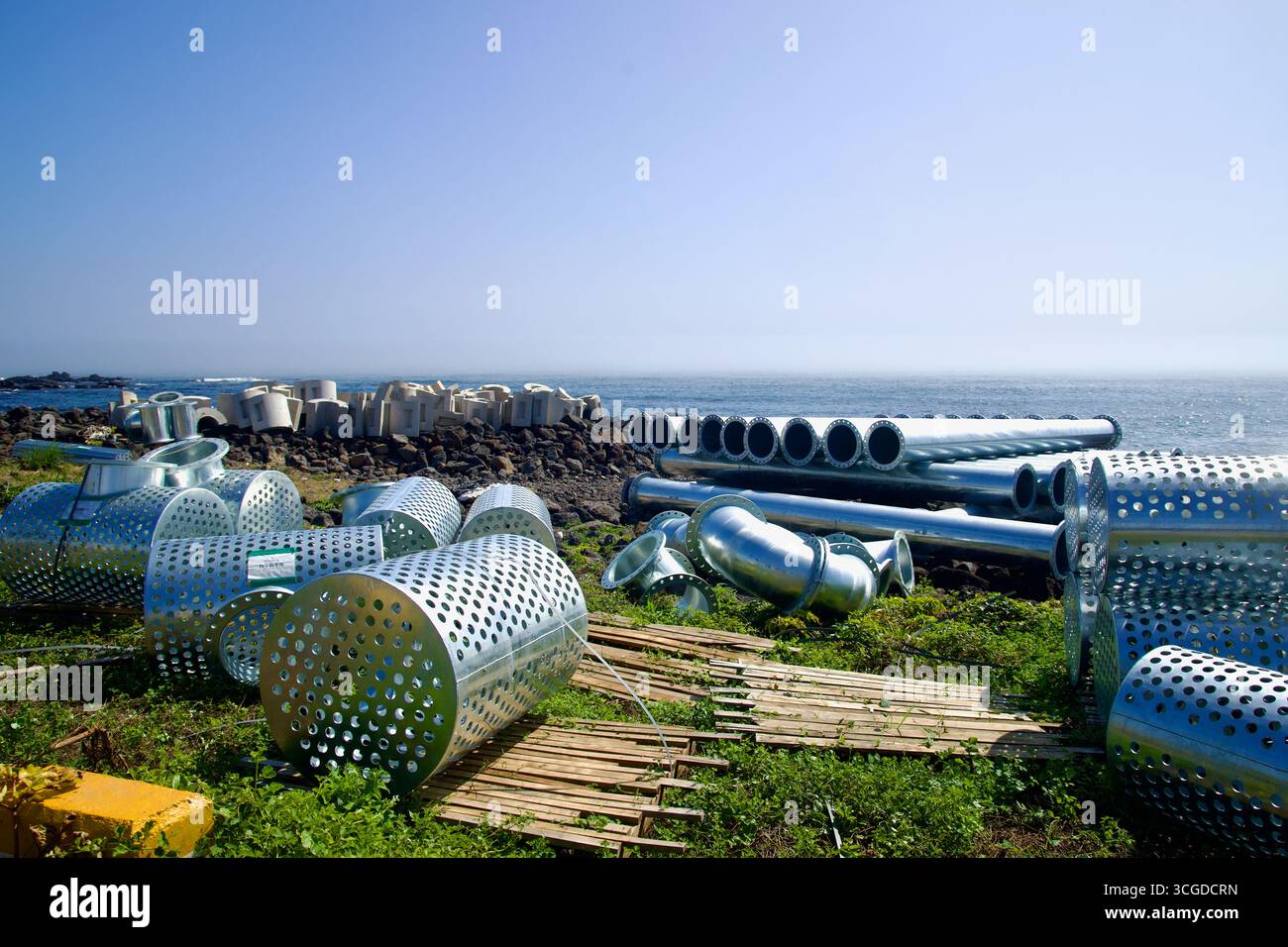 Pile di cilindri galvanizzati perforati e tubi lunghi si trovano sulla riva accanto ai tetrapodi a Yeongnak, materiali allestiti per lavori costieri lungo Jeju» Foto Stock