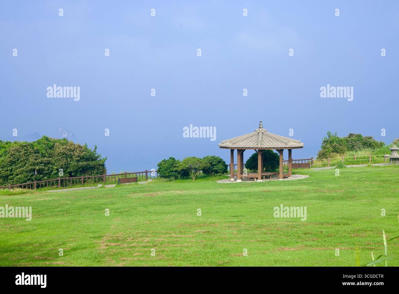 Un padiglione in legno sorge su un ampio prato che si affaccia sul mare in un parco in cima a una collina vicino a Songaksan sull'Isola di Jeju, con ringhiere e arbusti lungo il bordo. Foto Stock