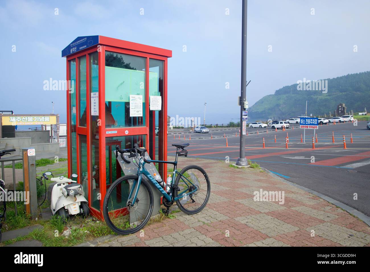 Una bicicletta da turismo si trova accanto allo stand rosso Korea Cycling Road Certification Center di Songaksan, affacciato sull'area parcheggio e sul promontorio di Jeju Foto Stock