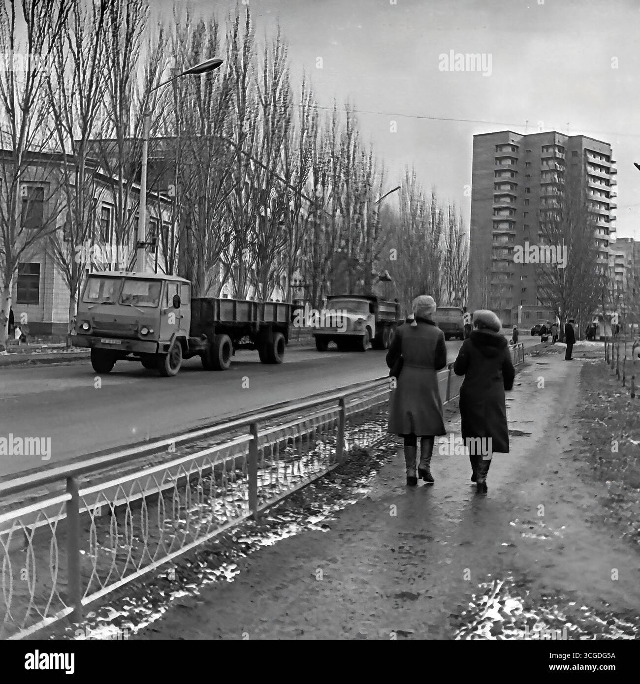 Una fotografia archivistica in bianco e nero della vita cittadina di Sloviansk all'inizio degli anni '1980, che cattura Svobody Street durante la bassa stagione con un flusso di camion e pedoni sovietici GAZ sullo sfondo di un nuovo edificio di nove piani, che riflette i contrasti della pianificazione urbana sovietica e la vita quotidiana dell'era della stagnazione, che serve come un prezioso documento della vita pacifica nel Donbas prima della guerra Foto Stock