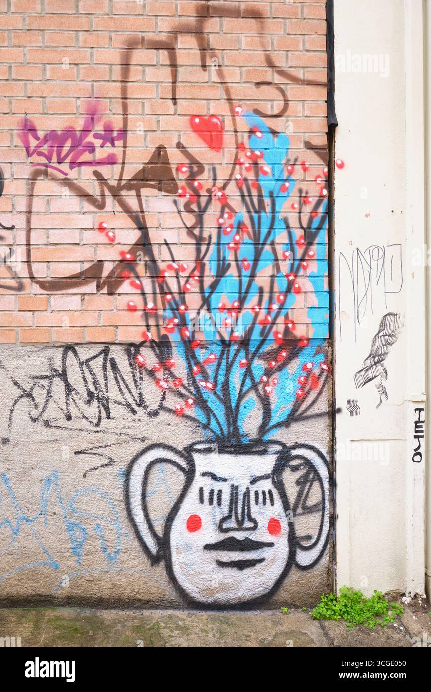 Un vaso di fiori bianco con una faccia divertente, fiori che escono, in fiore. Su un muro, Street art, graffiti a Bologna, Italia. Foto Stock