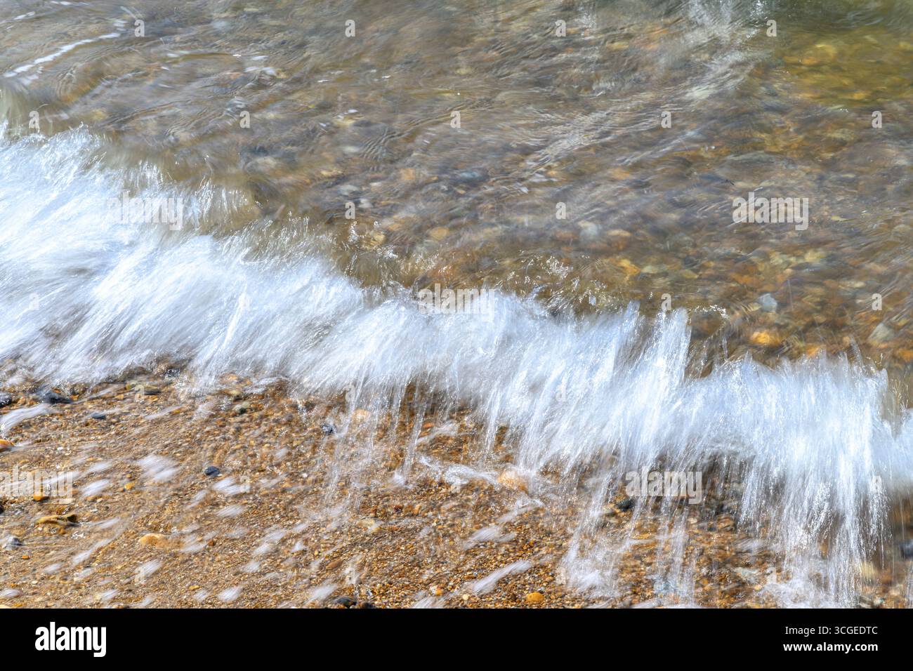 Onde sfocate sulla spiaggia di ciottoli e ciottoli a Whitstable, sulla costa del Kent settentrionale. Un'esposizione lunga produce l'effetto sfocato. Foto Stock