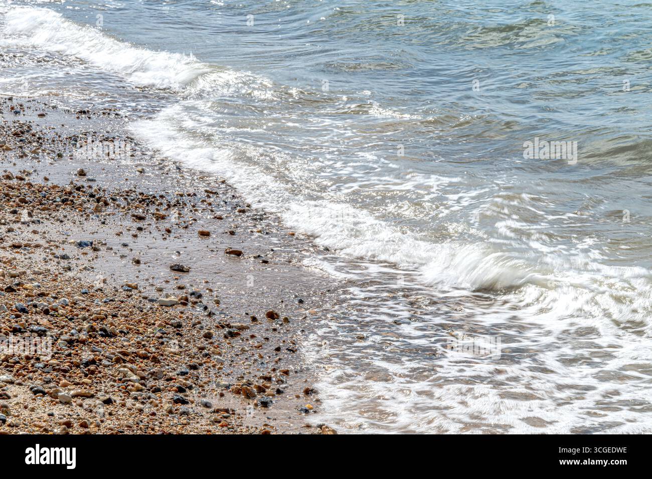 Onde sfocate sulla spiaggia di ciottoli e ciottoli a Whitstable, sulla costa del Kent settentrionale. Un'esposizione lunga produce l'effetto sfocato. Foto Stock