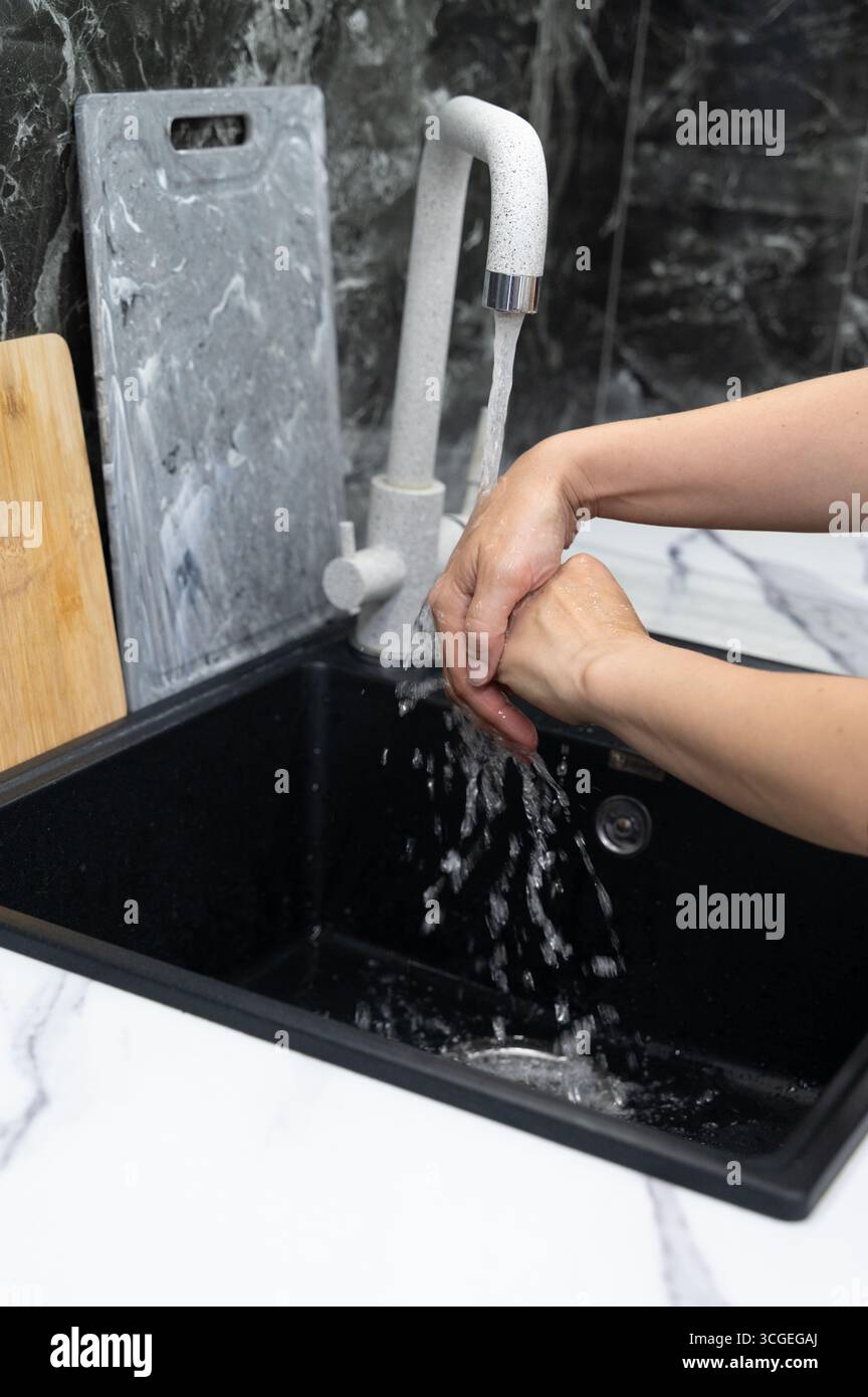Una persona che lava le mani su un elegante lavandino della cucina, sottolineando la pulizia e l'estetica moderna della cucina. Foto Stock