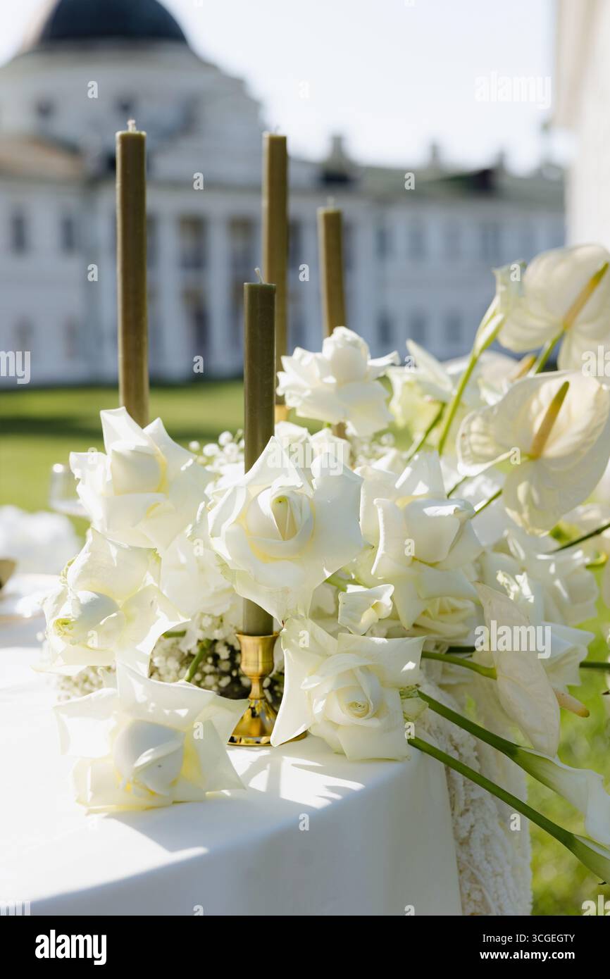 Un'incredibile esposizione di rose bianche e delicate fioriture esalta la bellezza di un raffinato ambiente esterno. Le candele alte si stagliano con grazia, illuminando Foto Stock
