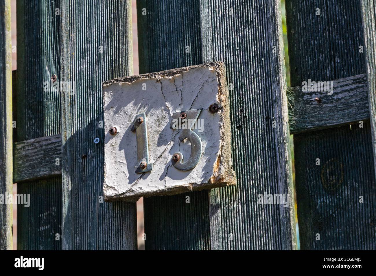 Un numero civico "13" con vernice sbucciante è apposto su una vecchia recinzione in legno testurizzato, catturando un'estetica rustica e invecchiata. Foto Stock