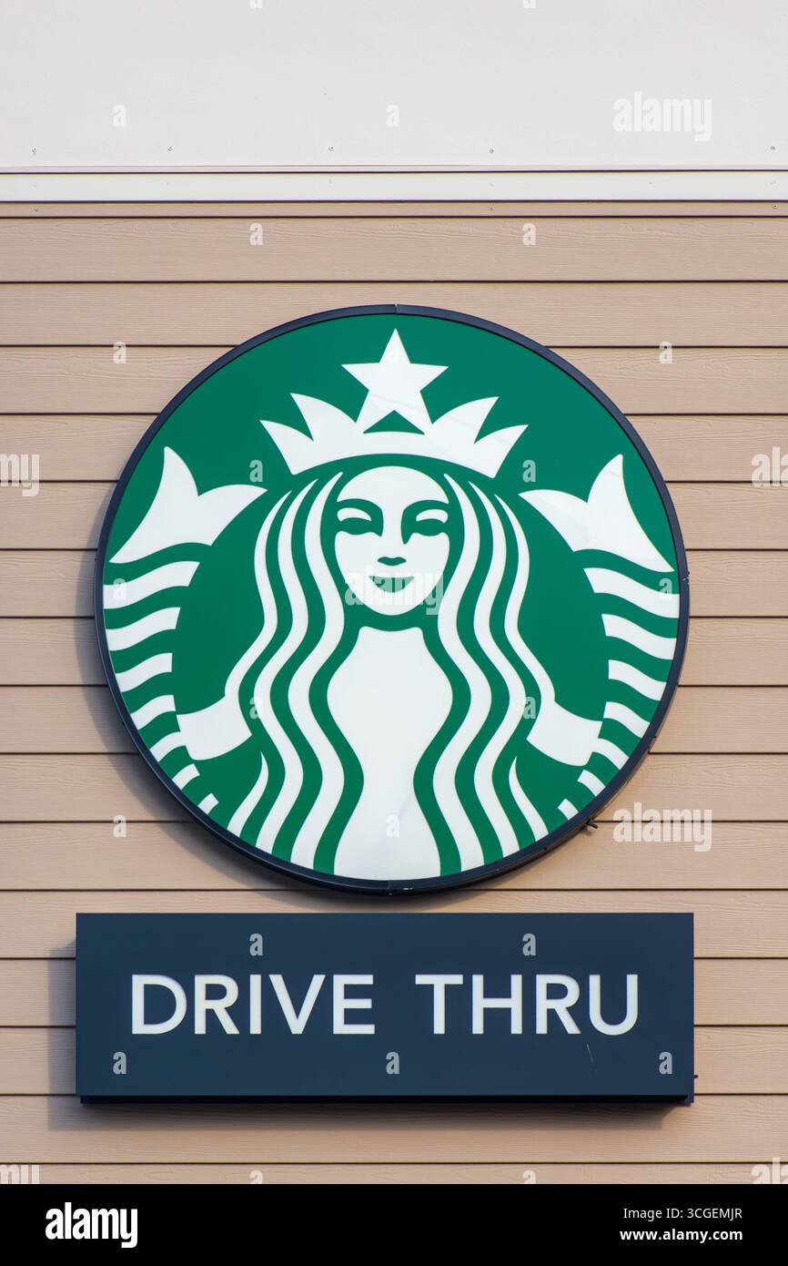Logo Starbucks e cartello drive-thru montati su una parete esterna con pannelli di legno marrone chiaro. Foto Stock