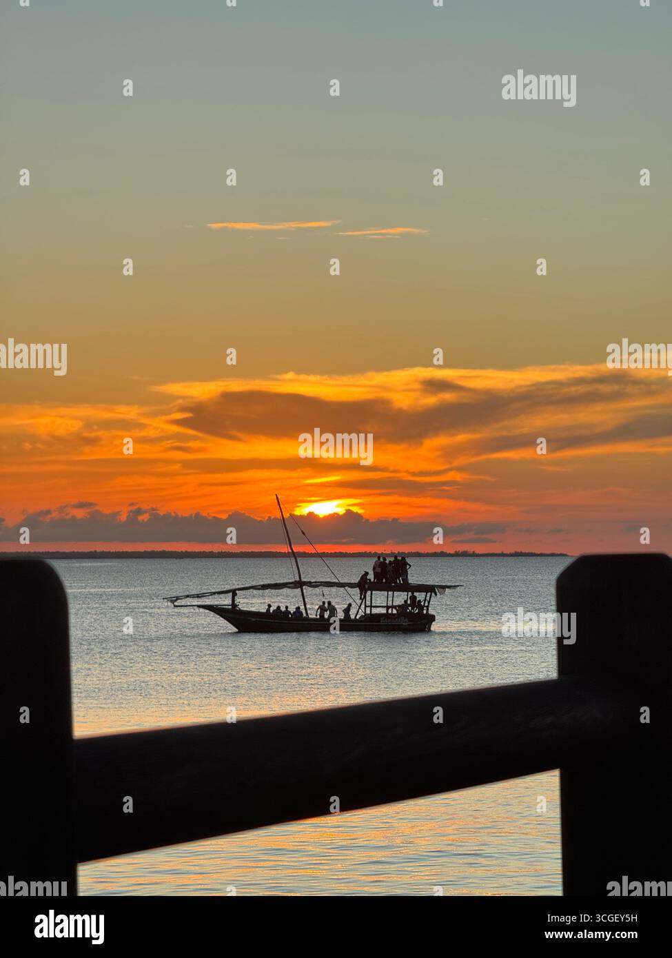 Il brillante tramonto arancione illumina l'orizzonte sopra le calme acque oceaniche di Zanzibar, Tanzania, creando un tranquillo paesaggio marino tropicale e una serena vista serale - Immagine stock catturata con smartphone