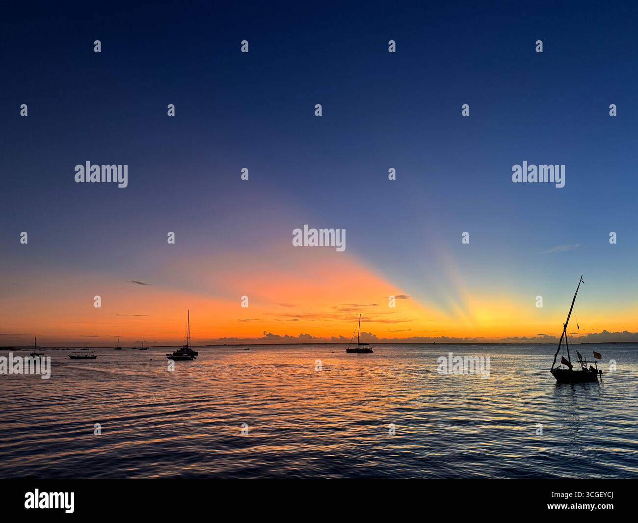 Barca tradizionale a vela al tramonto dorato sulle calme acque oceaniche di Zanzibar, Tanzania, che offre un tranquillo paesaggio marino e una romantica scena di vacanza tropicale - Immagine stock catturata con smartphone