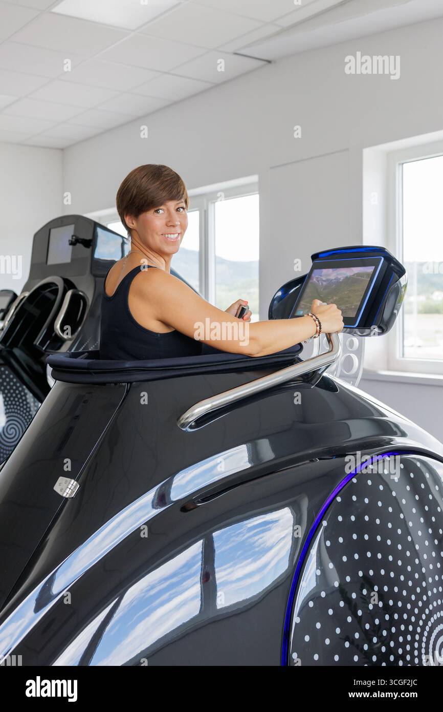 Donna felice che utilizza una capsula del tapis roulant sottovuoto avanzata con riscaldamento a infrarossi per cardiofitness, dimagrimento e benessere in una moderna sala fitness. Foto Stock