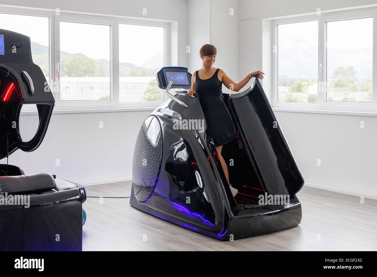 Donna sorridente entra nell'innovativa capsula del tapis roulant sottovuoto con riscaldamento a infrarossi, progettata per i benefici cardio, dimagrante e per la cura della pelle in una moderna Foto Stock
