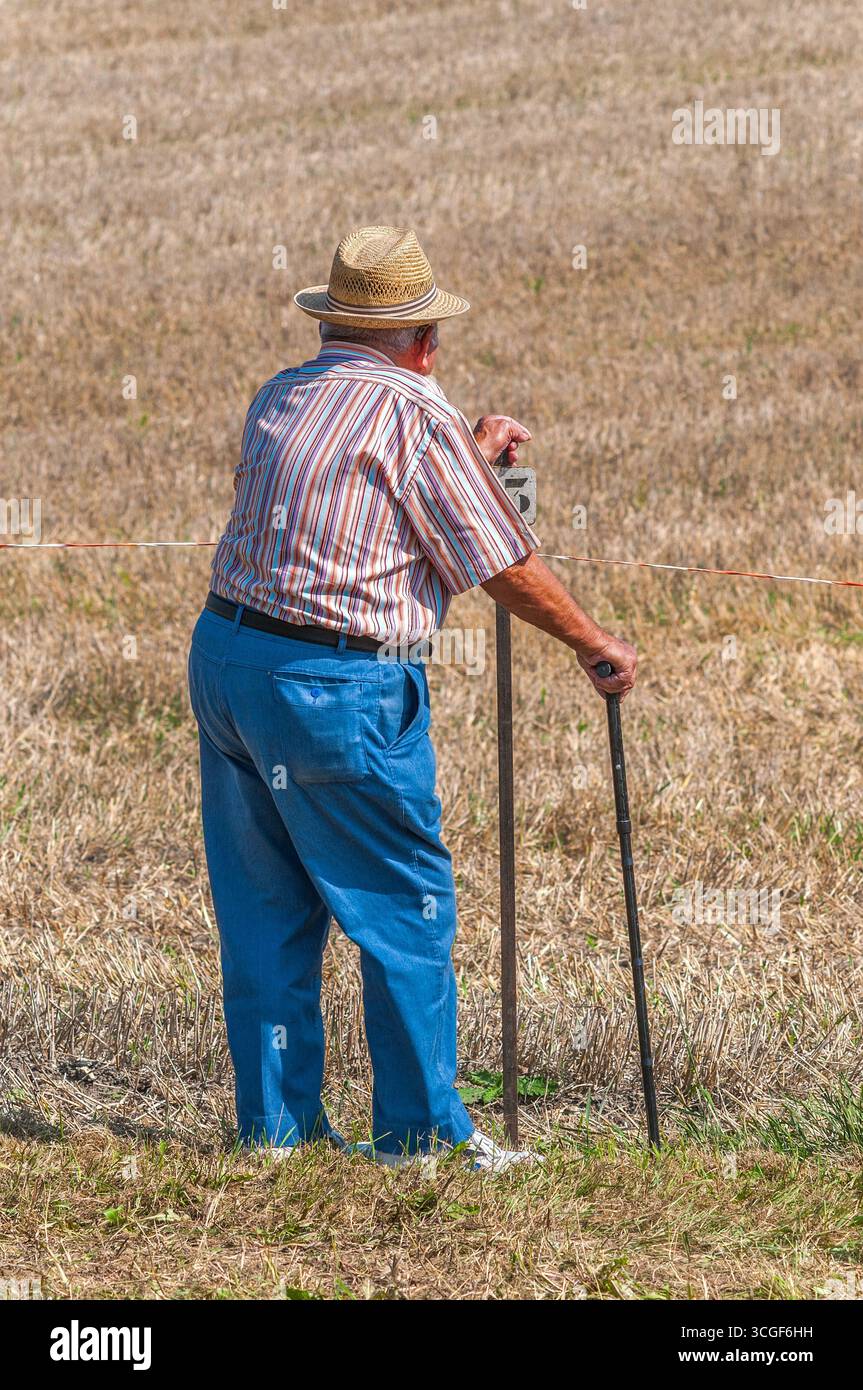 Contadino in pensione vestito in modo intelligente con bastone da passeggio che guarda attraverso i terreni agricoli - Châtillon-sur-Indre, Indre (36), Francia. Foto Stock