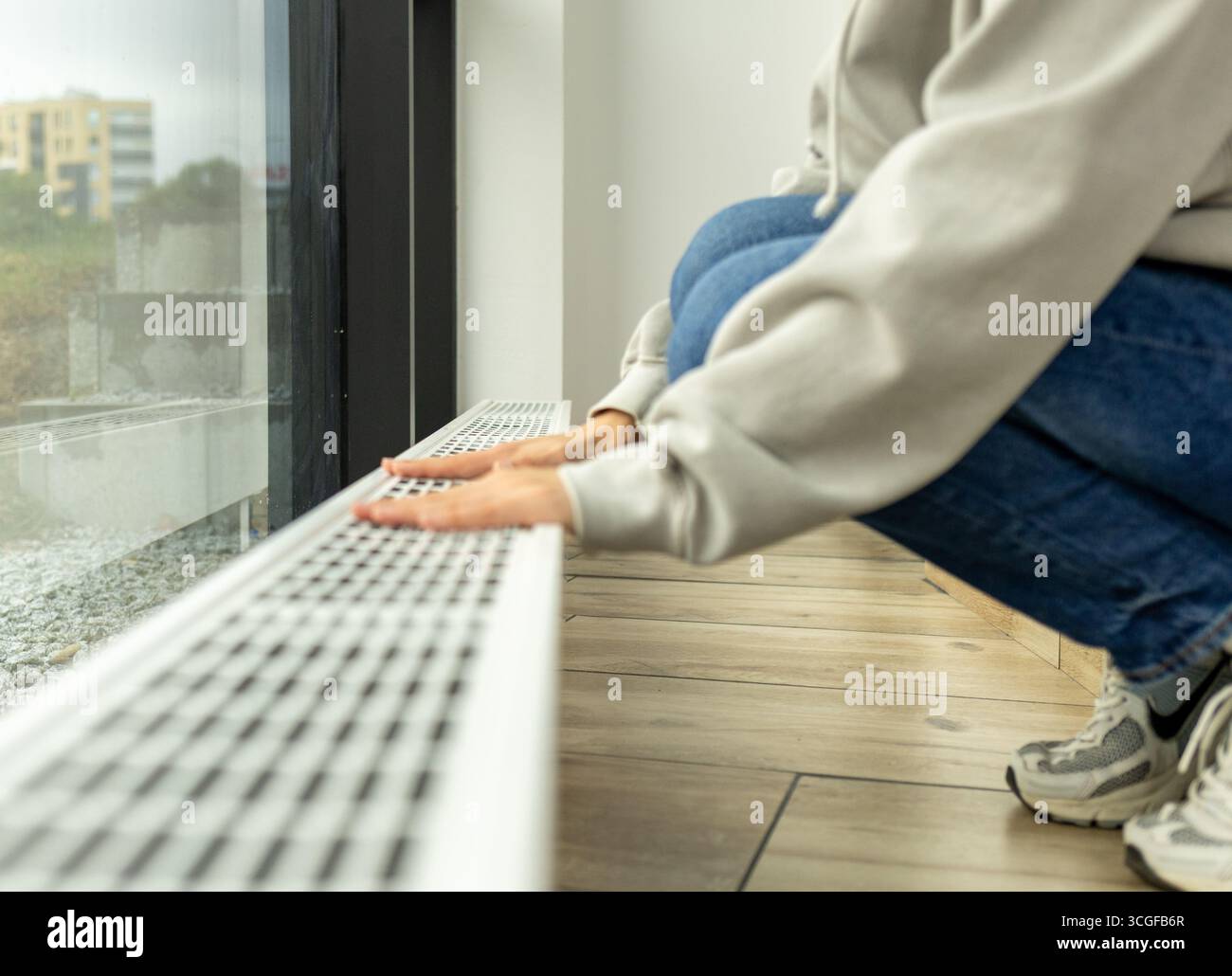 radiatore di riscaldamento nell'appartamento, la persona porta le mani in un maglione caldo al radiatore per controllare quanto caldo.costi di riscaldamento e utenze in inverno Foto Stock