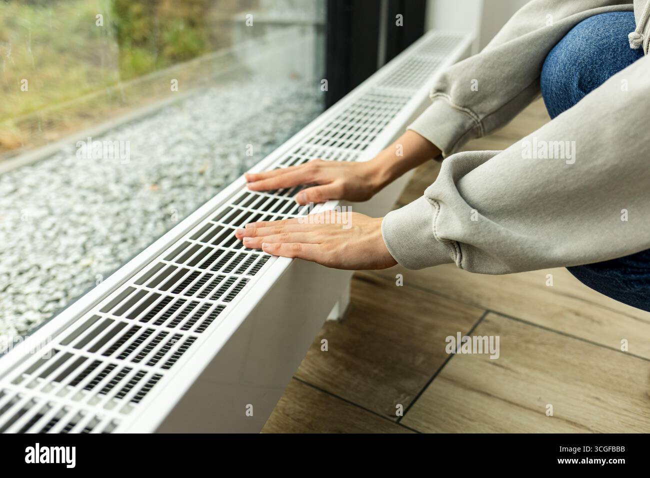 radiatore di riscaldamento nell'appartamento, la persona porta le mani in un maglione caldo al radiatore per controllare quanto caldo.costi di riscaldamento e utenze in inverno Foto Stock