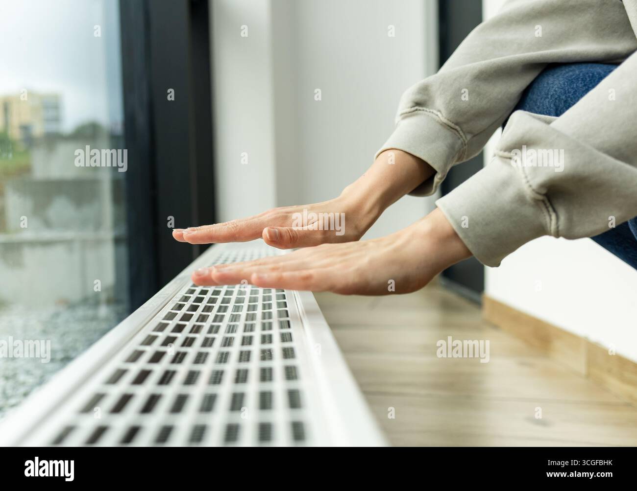 radiatore di riscaldamento nell'appartamento, la persona porta le mani in un maglione caldo al radiatore per controllare quanto caldo.costi di riscaldamento e utenze in inverno Foto Stock