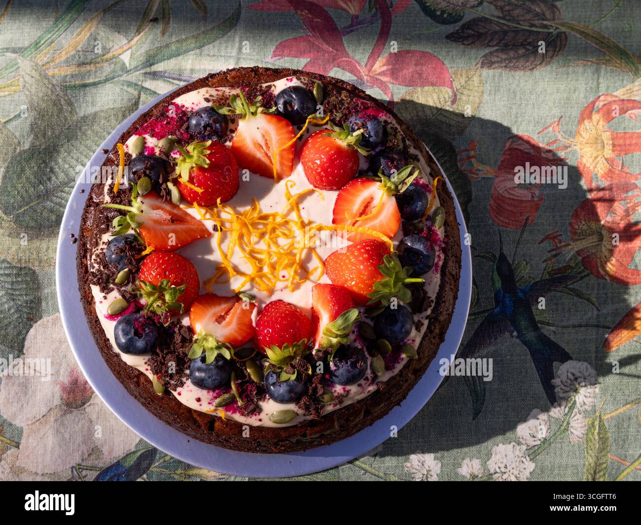 Vista dall'alto della torta di carote Zoe-friendly dal Tim Spector's Food for Life, condita con fragole, mirtilli, scorza d'arancia e fiori commestibili. � Foto Stock Vista dall'alto della torta di carote Zoe-friendly dal Tim Spector's Food for Life, condita con fragole, mirtilli, scorza d'arancia e fiori commestibili. � Foto Stock