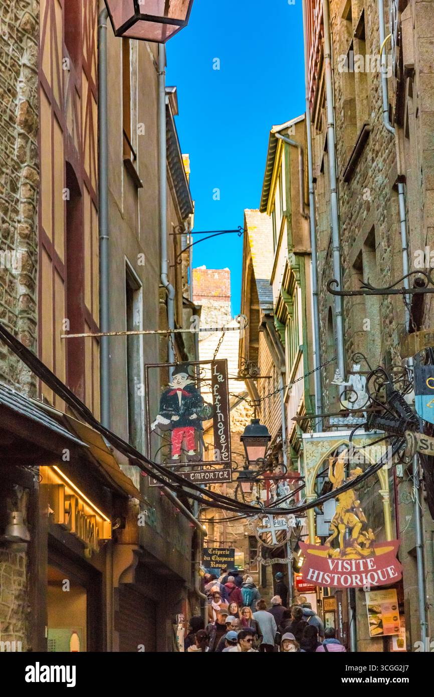 Bella vista dei cartelli decorati che sovrastano la folla affollata lungo la strada principale di Mont-Saint-Michel, grande Rue. In ferro battuto o intagliato... Foto Stock