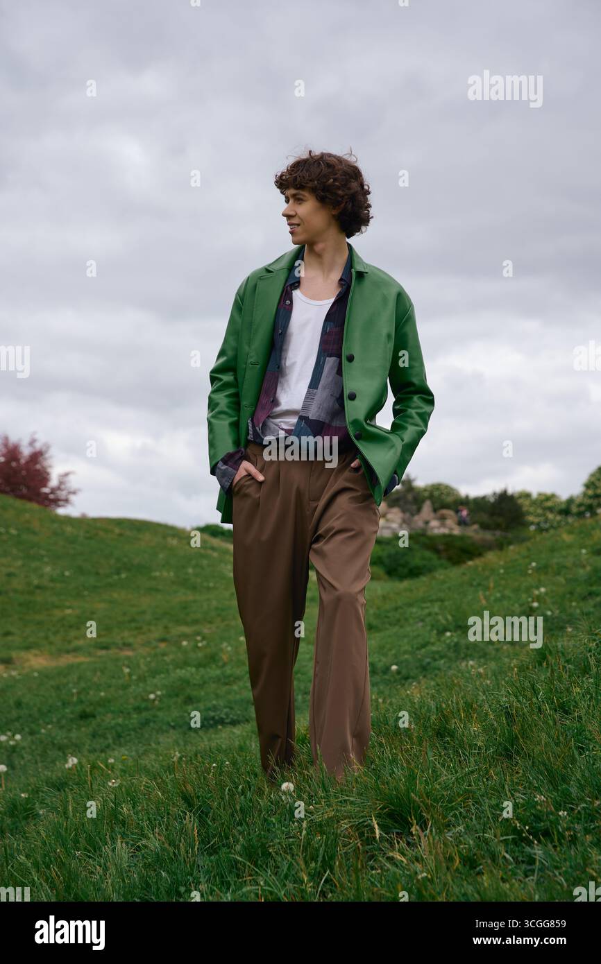 Uno studente affascinante passeggia attraverso un vivace paesaggio verde, abbracciando un momento di tranquillità all'aperto. Foto Stock