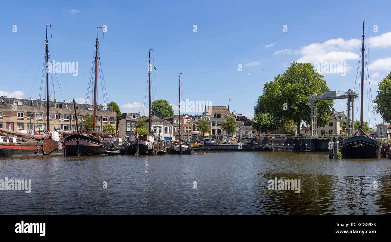 Le tradizionali barche a vela olandesi sono ormeggiate lungo un pittoresco canale di Gouda, con edifici storici e un ponte levatoio sotto un cielo blu. Foto Stock