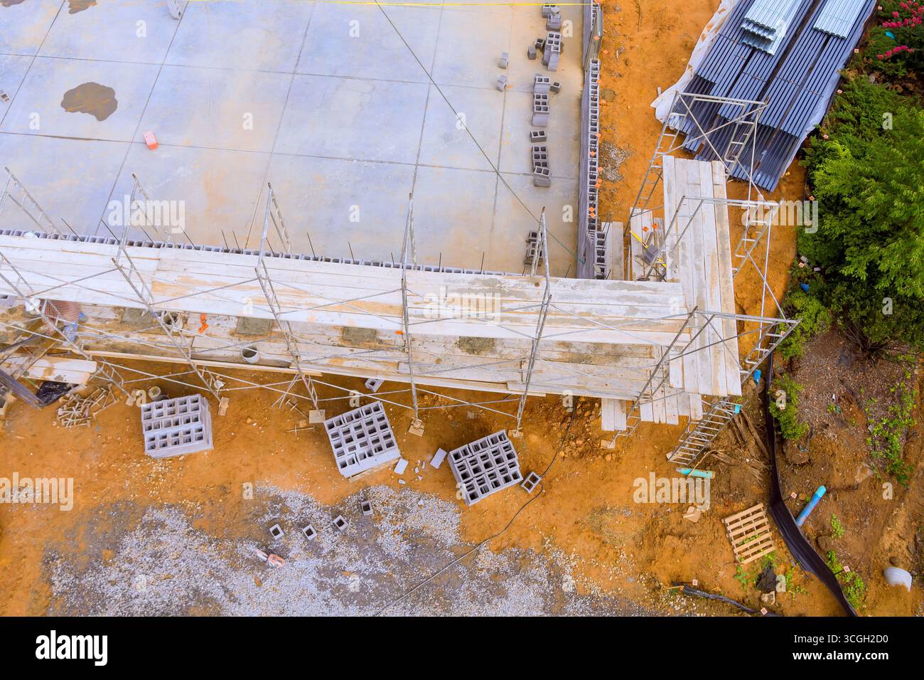 L'impalcatura circonda una struttura parzialmente costruita, con materiali da costruzione sparsi intorno, giornata di lavoro attiva Foto Stock