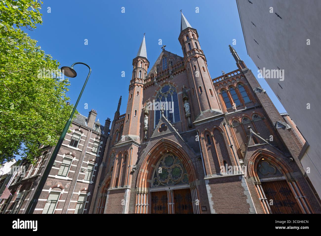 Una magnifica chiesa in mattoni rossi 'De Gouwekerk' con due guglie prominenti si innalza maestosamente contro un cielo azzurro luminoso, mostrando intricati Revi gotici Foto Stock