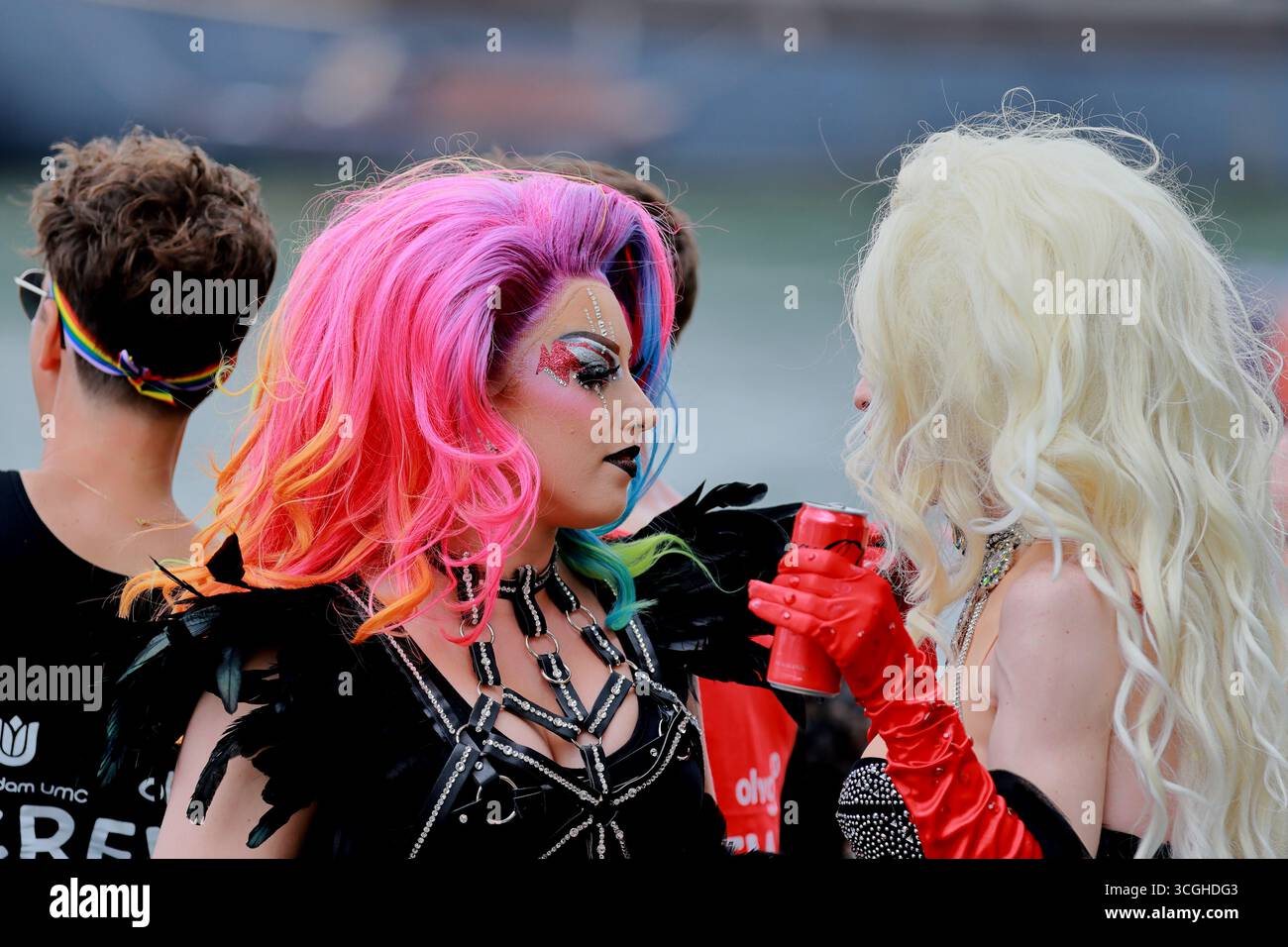 Due artisti di drag-performer si affrontano in una conversazione, uno con i capelli arcobaleno, durante la Pride Amsterdam Canal Parade ad Amsterdam, Paesi Bassi, vicino all'acqua. Foto Stock
