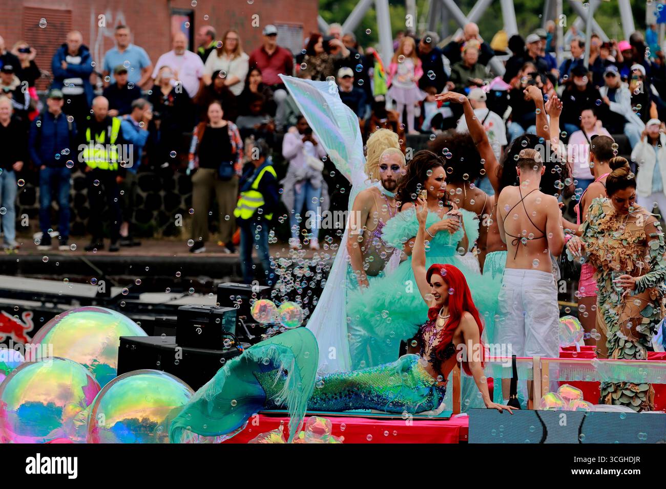 Interpreti in costume con sirena e bollicine su una sfilata di canali Pride Amsterdam, Amsterdam, Paesi Bassi, con spettatori sulla banchina della città. Foto Stock