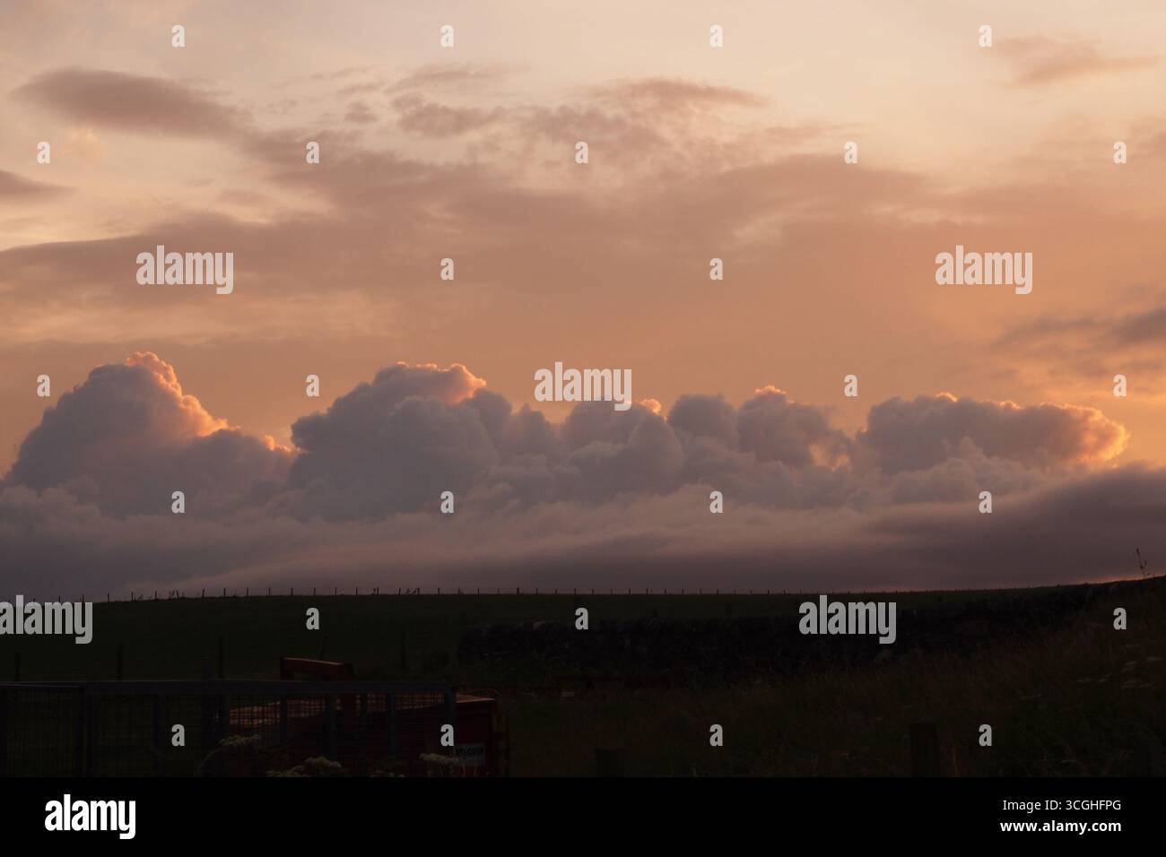Un tramonto sulle fattorie costiere di Islay, Ebridi interne, Scozia, Regno Unito, che mostra le minacciose nuvole di pioggia che si riuniscono nel bagliore dorato Foto Stock